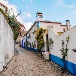 Obidos Portugal quaint street with cobblestone, whitewashed buildings with blue accents, and flowers